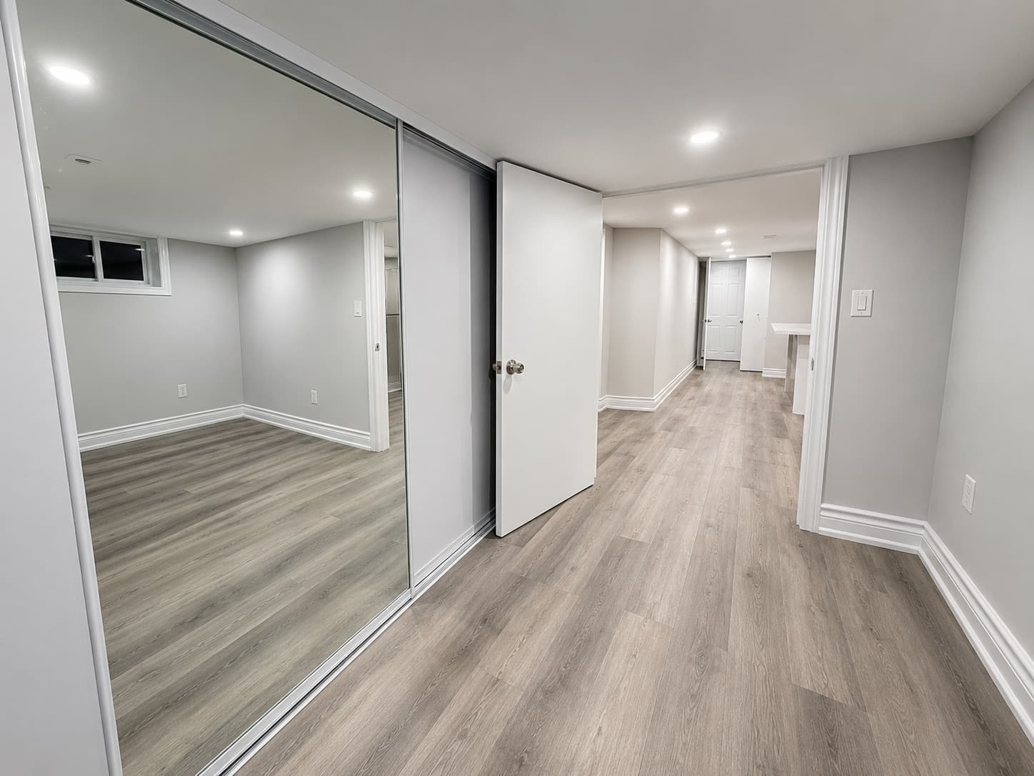 Finished basement renovation with grey walls, wood-look flooring, mirrored closet doors, and recessed lighting