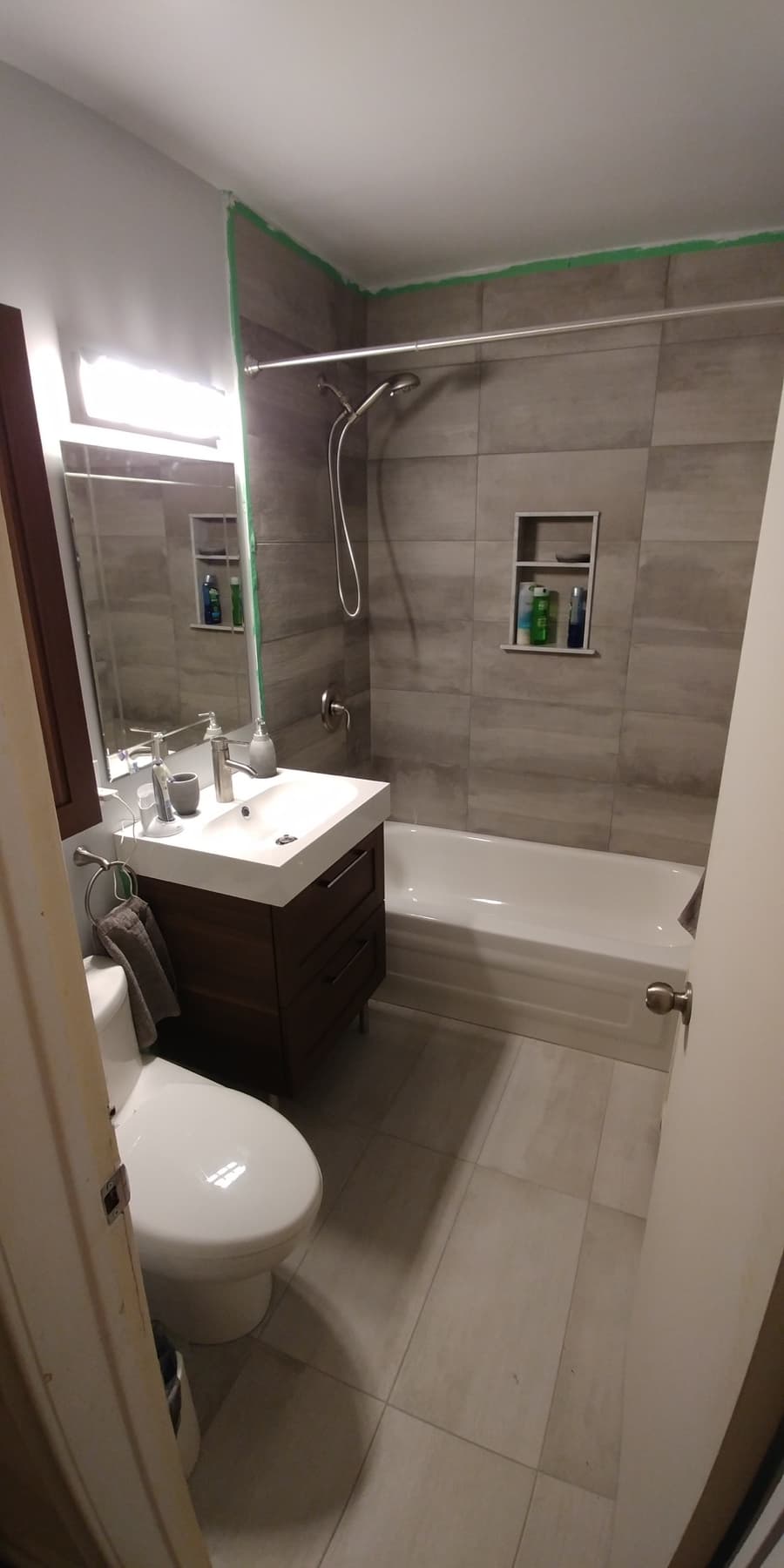 Bathroom renovation photo showing tiled shower area, vanity, toilet, and glass shower partition