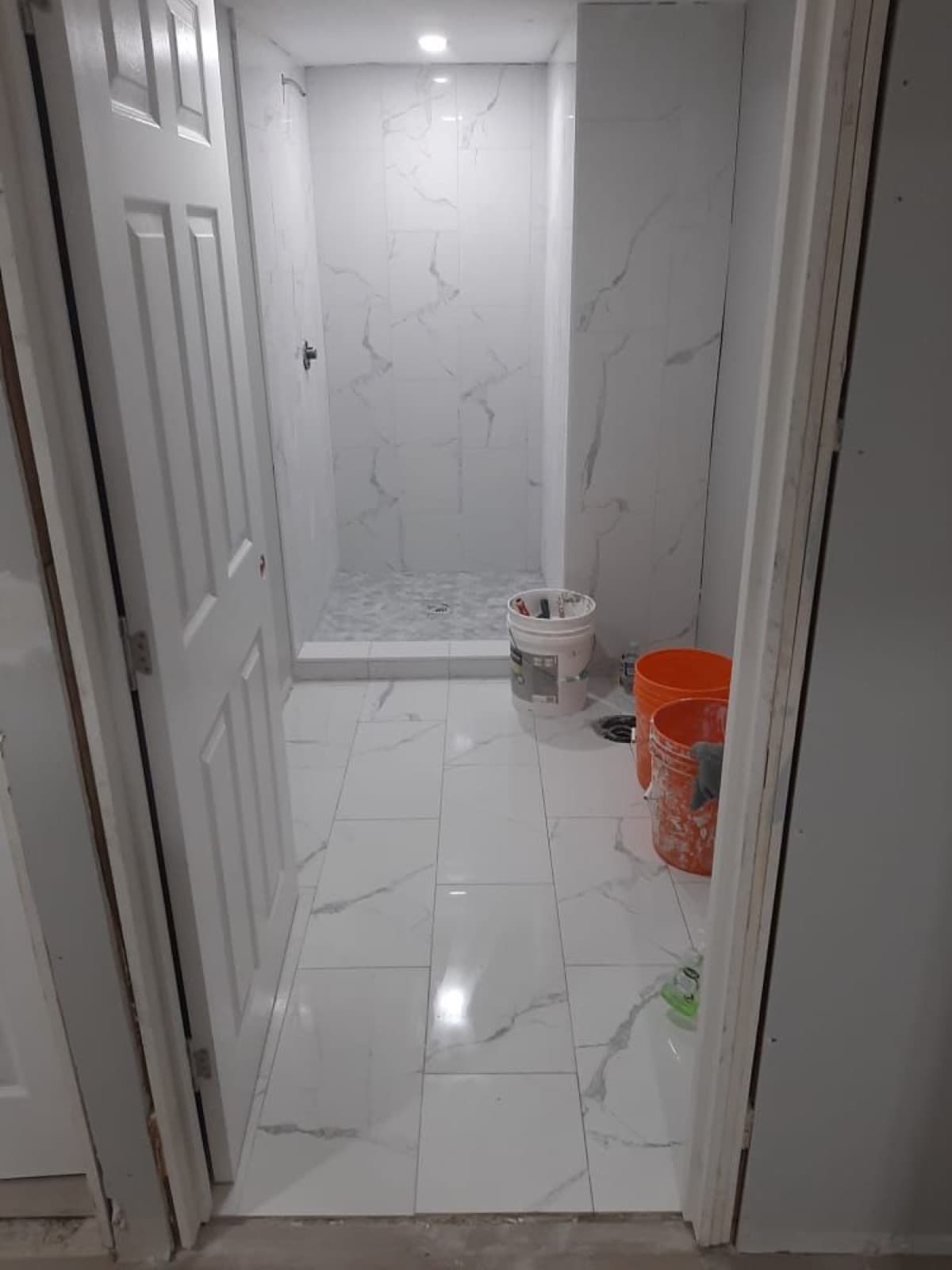 Bathroom renovation in progress with white marble-style shower tile and floor tile installation