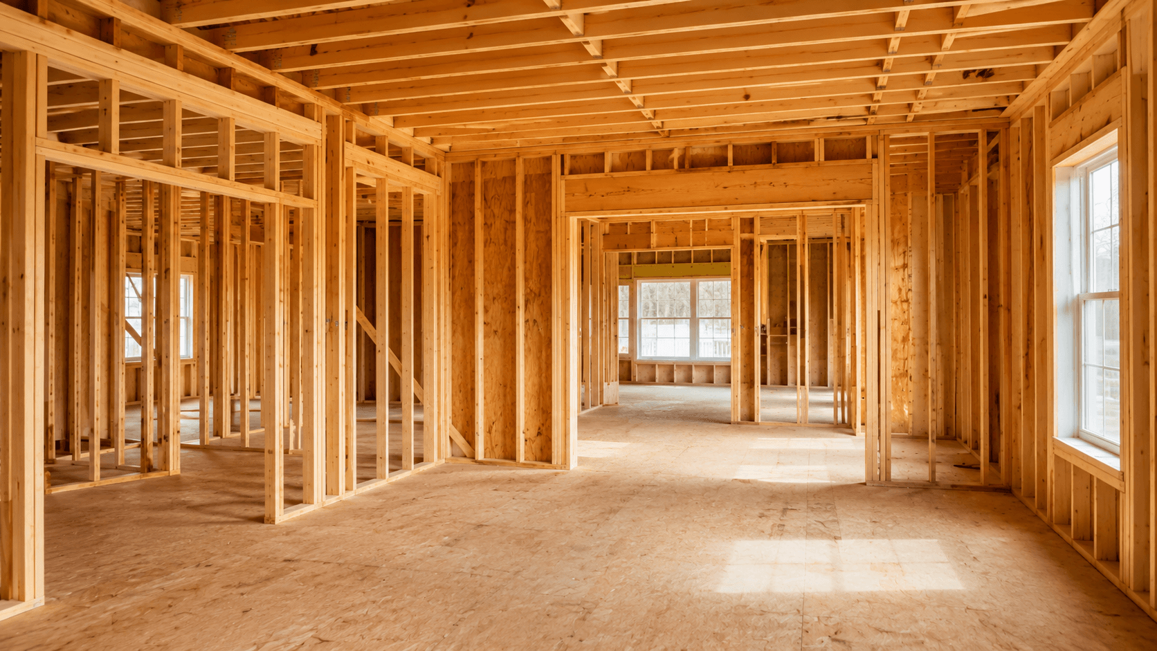 Interior wood framing for a residential renovation with open studs, ceiling joists, and window openings
