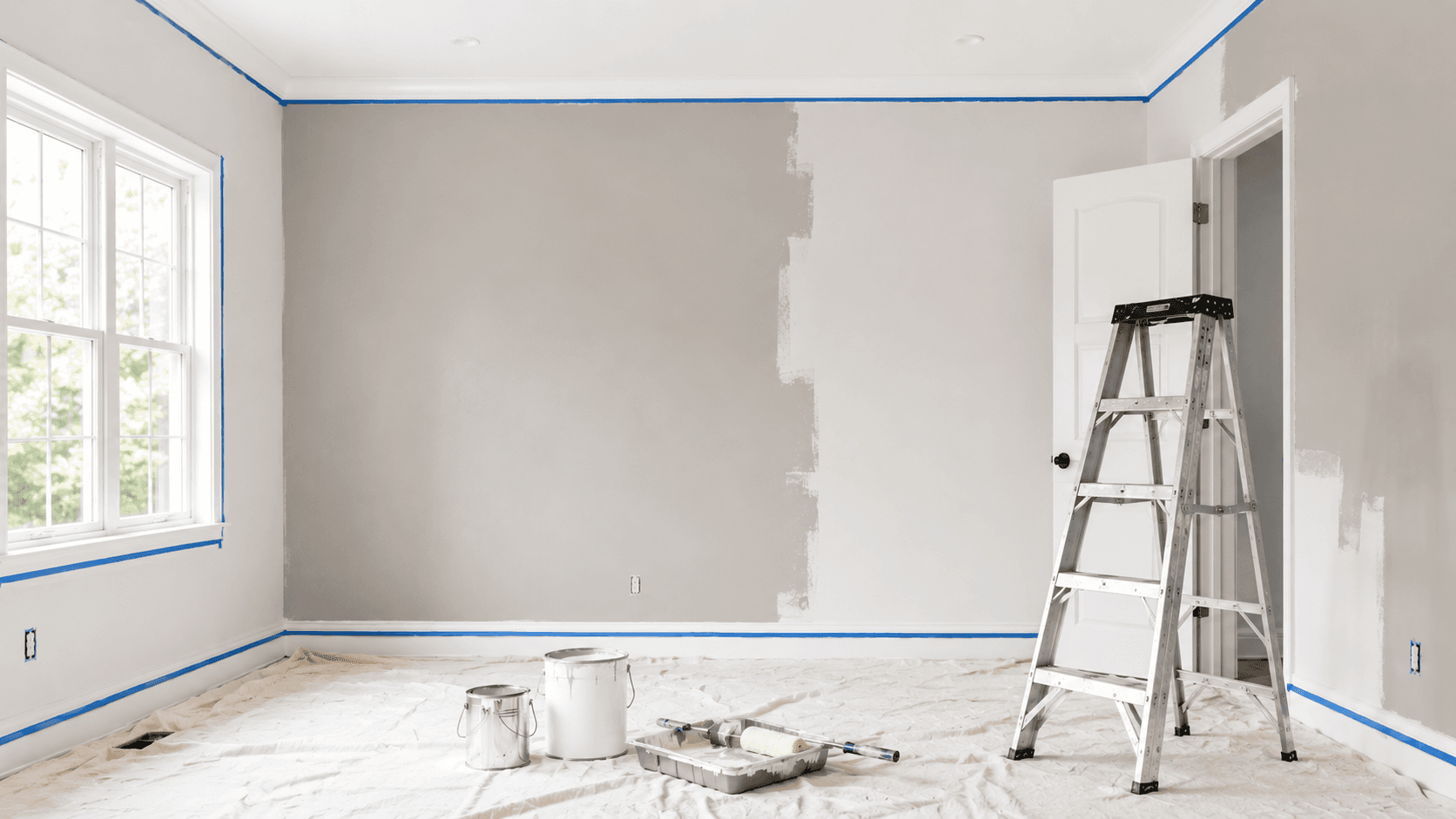 Interior room prepared for painting with taped trim, drop cloths, paint cans, and a ladder