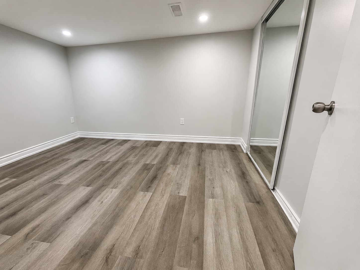 Finished flooring installation with wood-look plank flooring, grey walls, white trim, and mirrored closet doors