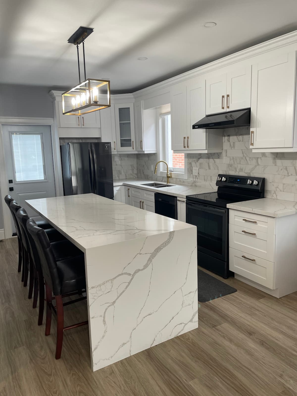 Kitchen renovation detail view showing white cabinetry, marble-style backsplash, island, lighting, and updated flooring