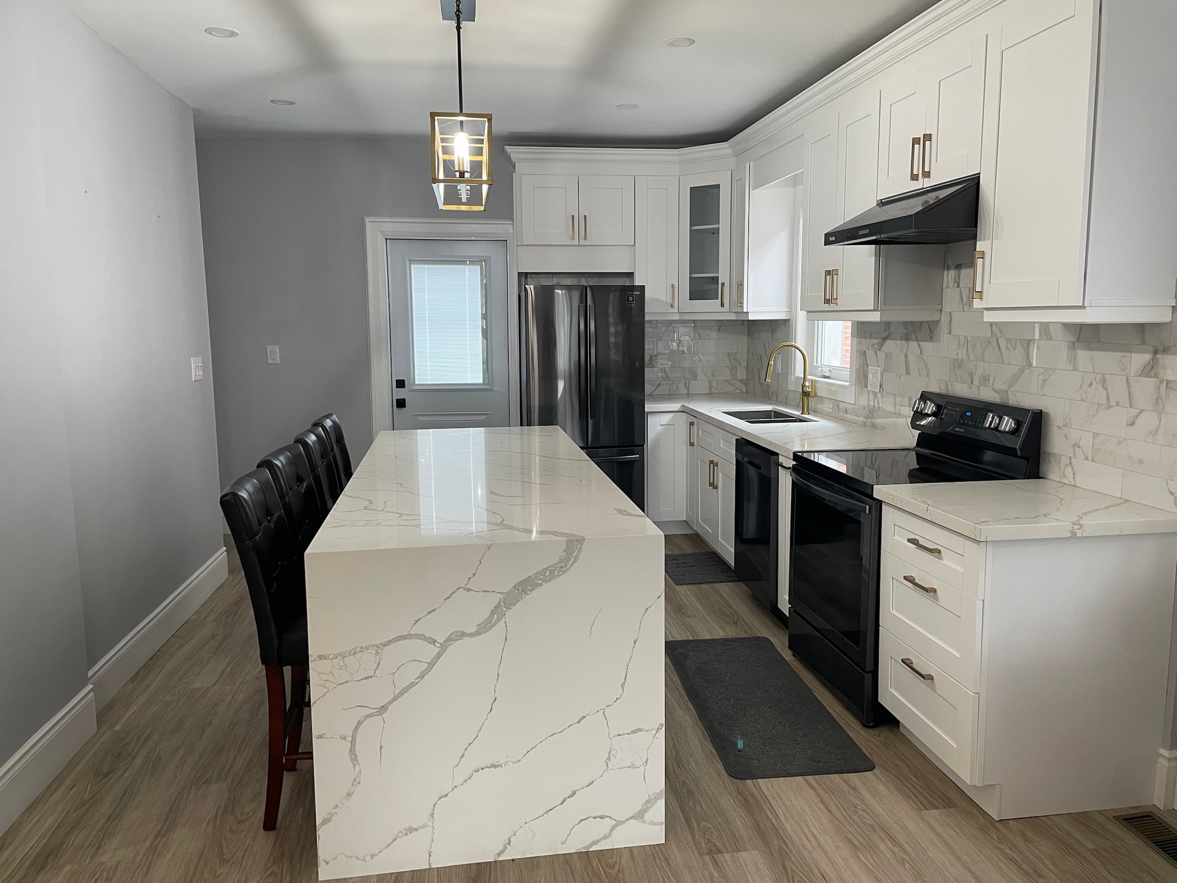 Finished kitchen renovation with white cabinetry, marble-style island, tile backsplash, and updated flooring